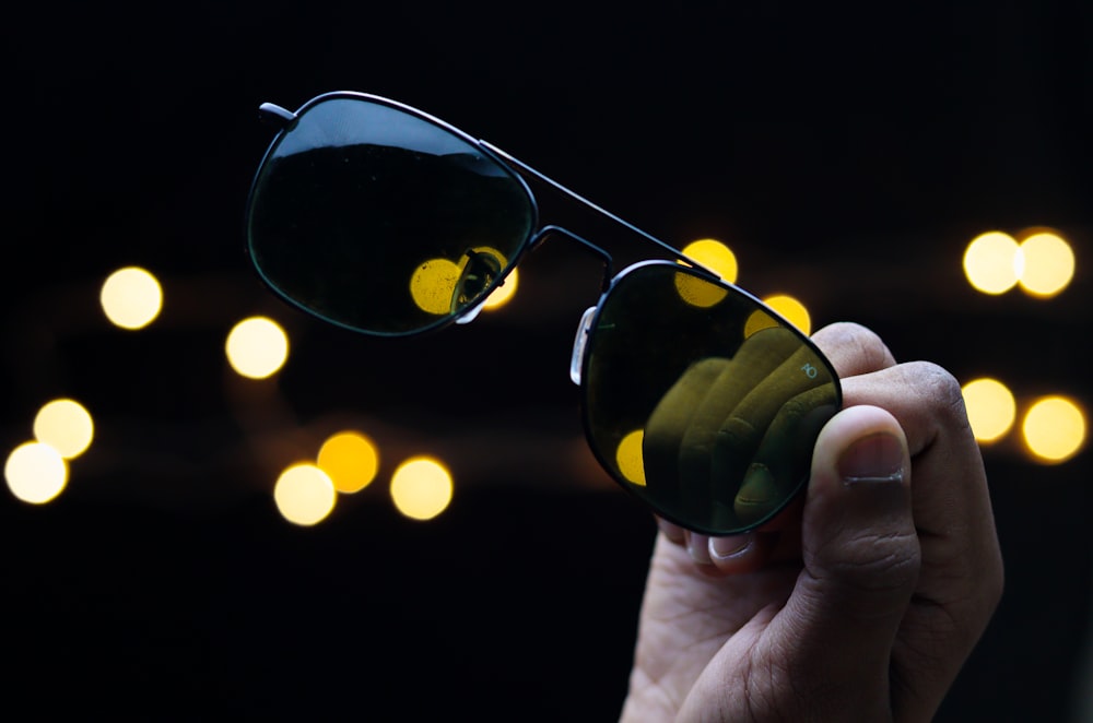 pessoa segurando óculos de sol verdes e pretos