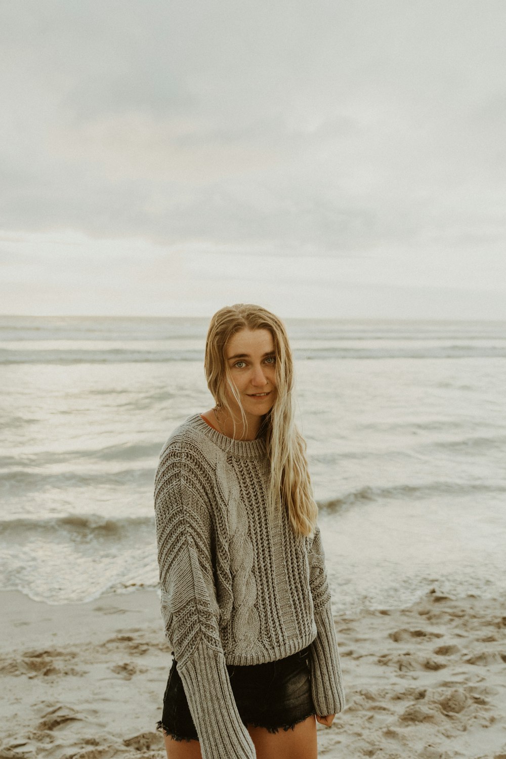 낮 동안 해변에 서 있는 흰색 니트 스웨터를 입은 여자