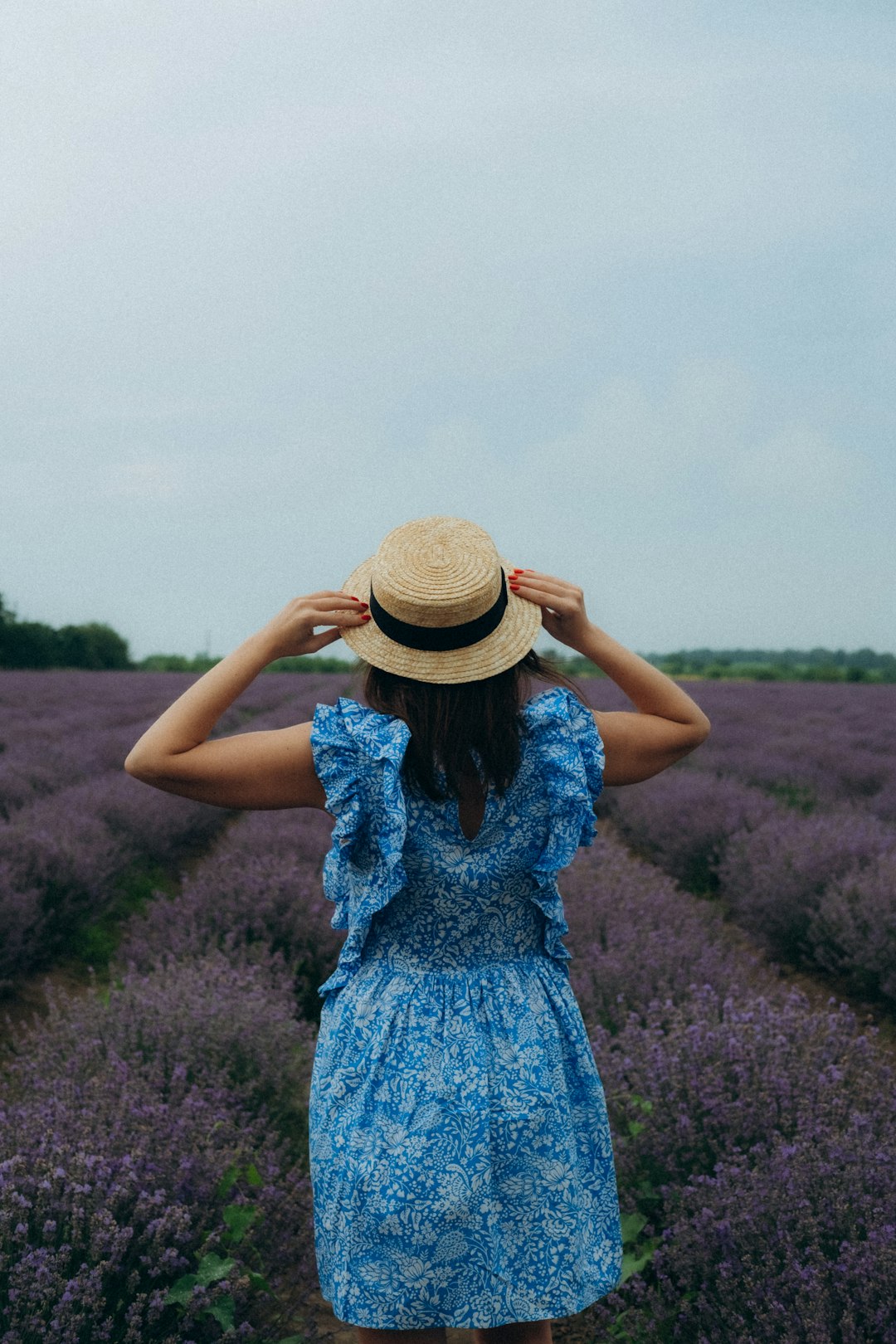 woman in blue and white floral dress wearing brown straw hat standing on purple flower field