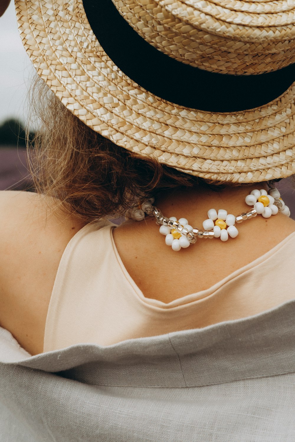 woman in white tank top wearing white pearl necklace and brown straw hat