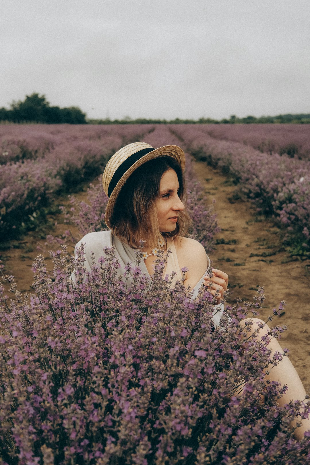 woman in white long sleeve shirt and white and black hat standing on purple flower field