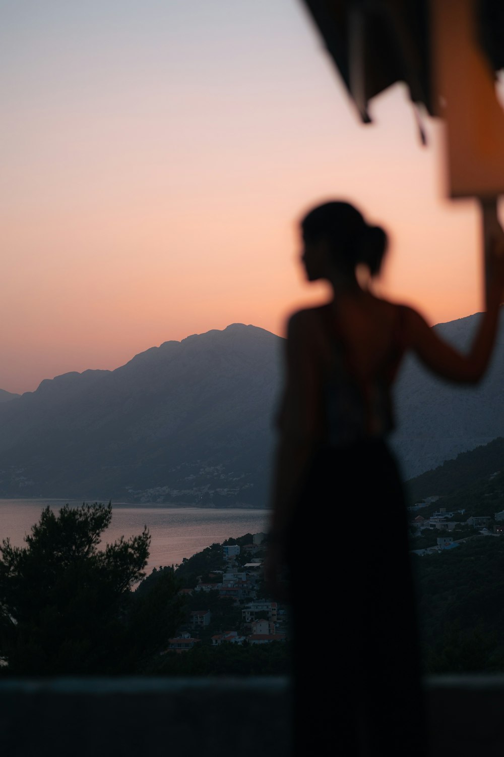 silhouette di donna in piedi sulla roccia vicino allo specchio d'acqua durante il tramonto