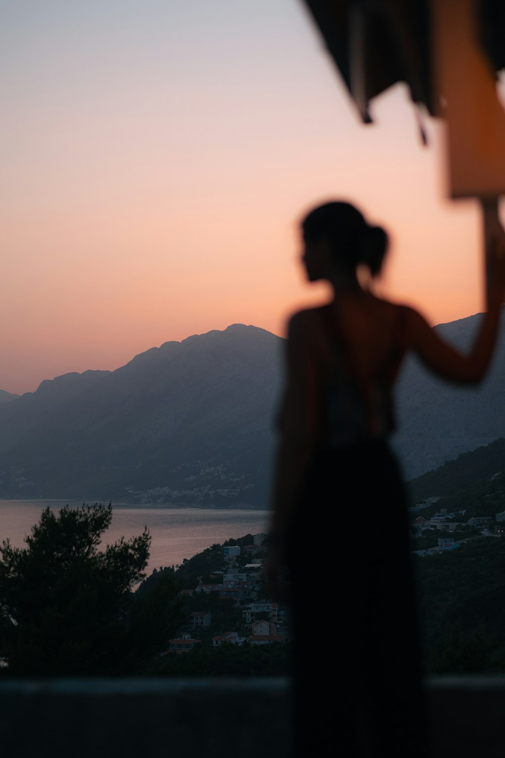 silhouette of woman standing on rock near body of water during sunset