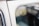 The image depicts a close-up view of a vintage car window, displaying its reflective glass surface. The interior and exterior details of the vehicle are blurred, creating a soft focus on the etched writing in the window that includes a logo and specifications.