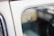 The image depicts a close-up view of a vintage car window, displaying its reflective glass surface. The interior and exterior details of the vehicle are blurred, creating a soft focus on the etched writing in the window that includes a logo and specifications.