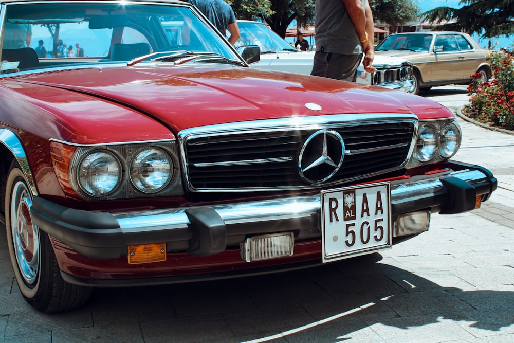 man in black jacket standing beside red car during daytime