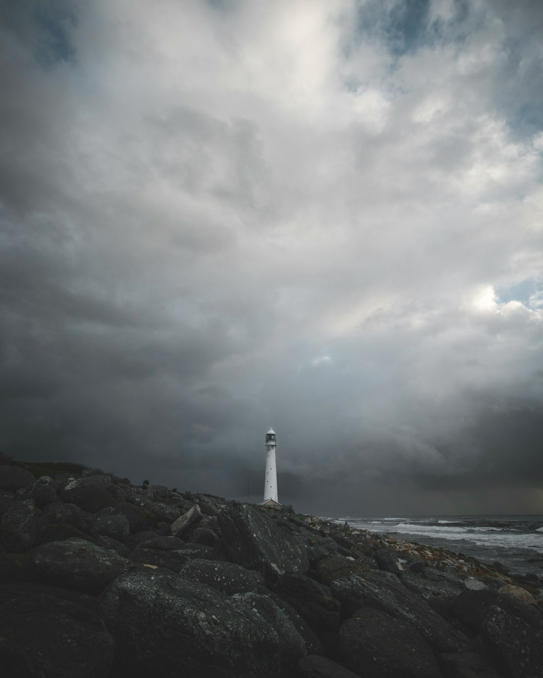 white and black lighthouse near body of water under cloudy sky