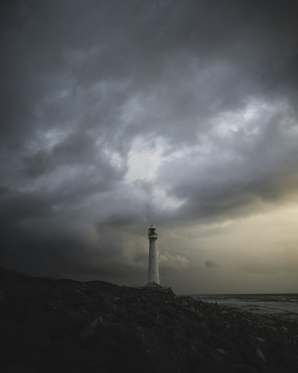 white lighthouse on brown rocky shore under white clouds