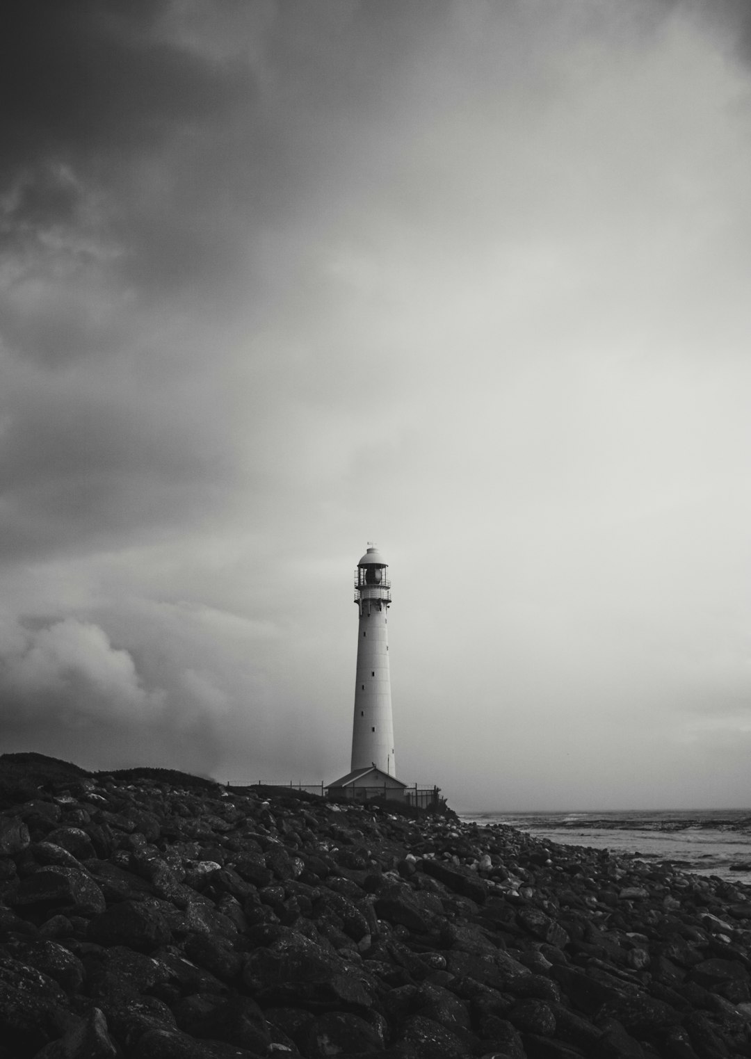 white and black lighthouse near body of water under cloudy sky