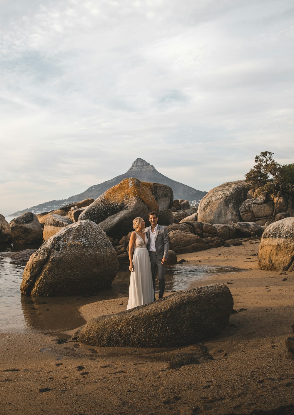 昼間、水辺の茶色の岩の上に立つ白いドレスを着た女性