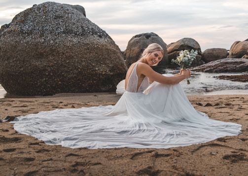 woman in white dress sitting on brown sand during daytime