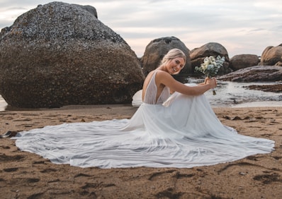 woman in white dress sitting on brown sand during daytime