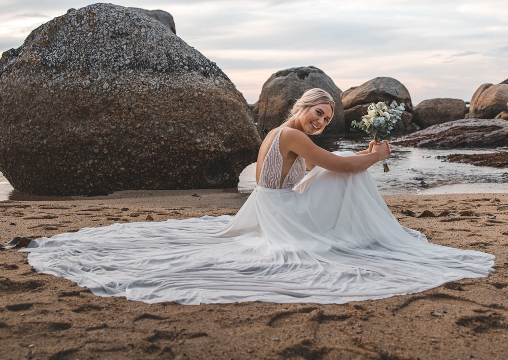 woman in white dress sitting on brown sand during daytime