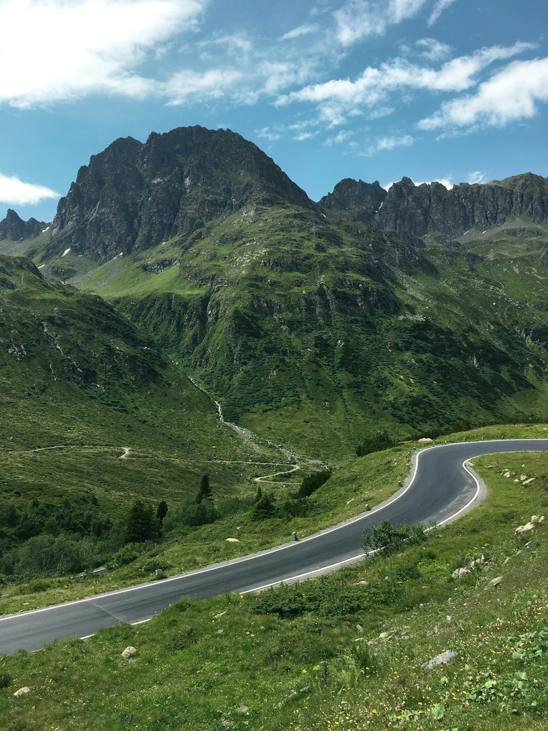 gray concrete road between green mountains during daytime