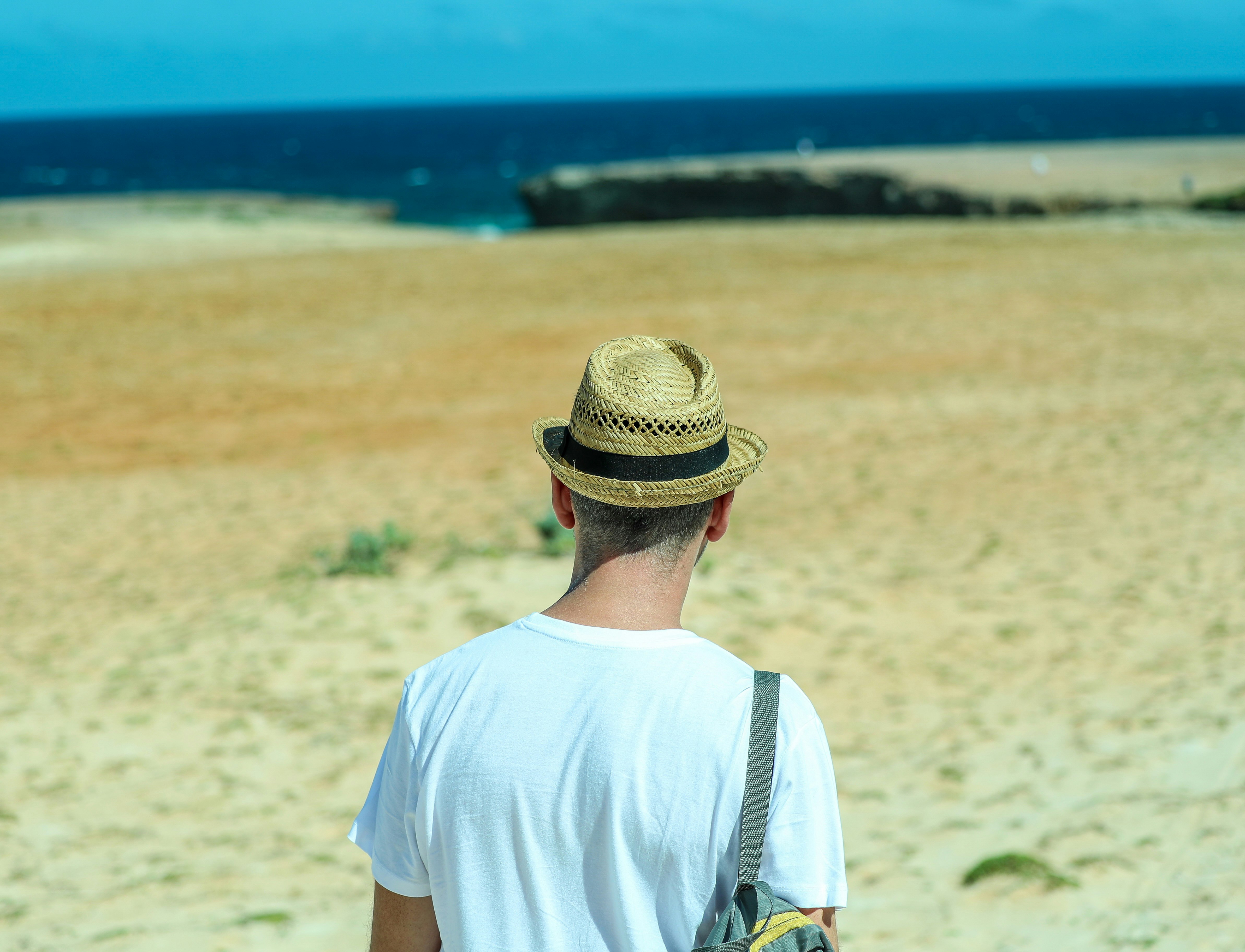 man in white crew neck t-shirt wearing brown hat standing on brown field during daytime