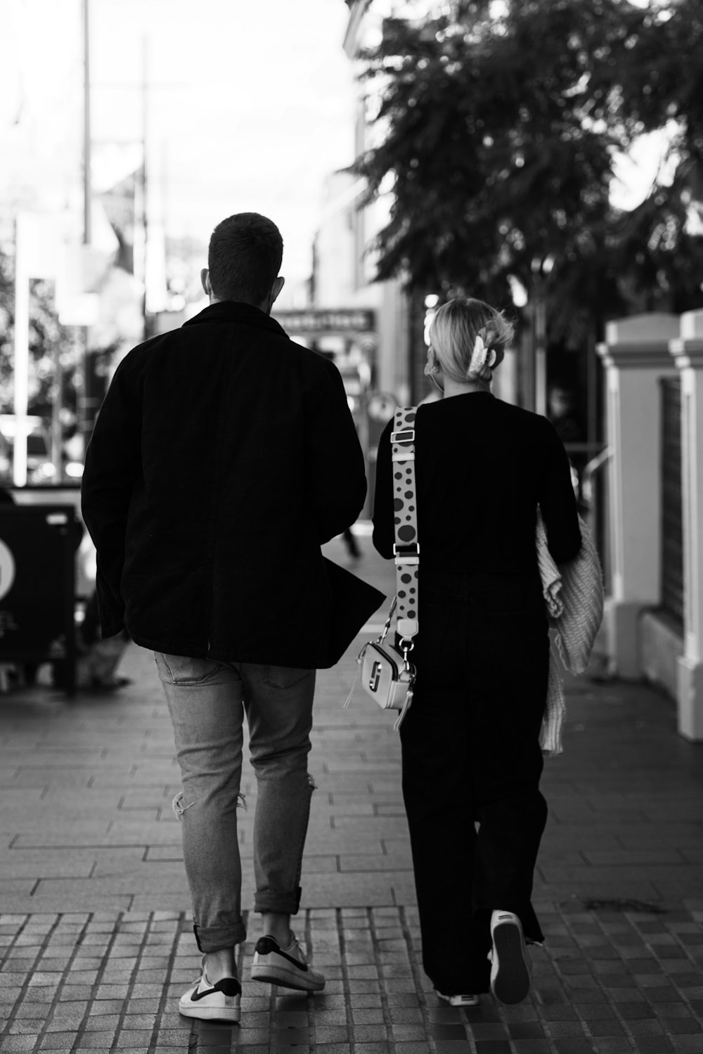 man and woman walking on sidewalk in grayscale photography