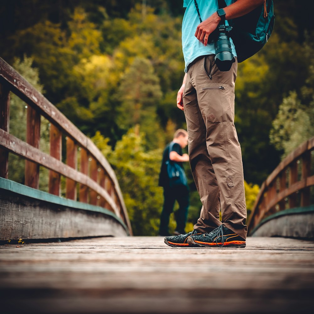 man in blue shirt and brown pants walking on bridge during daytime