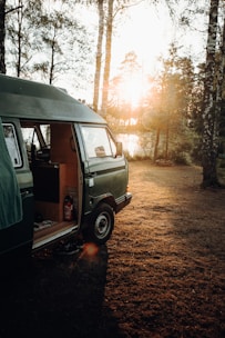 A cozy van parked in a forest clearing at sunset, with warm light glowing inside.