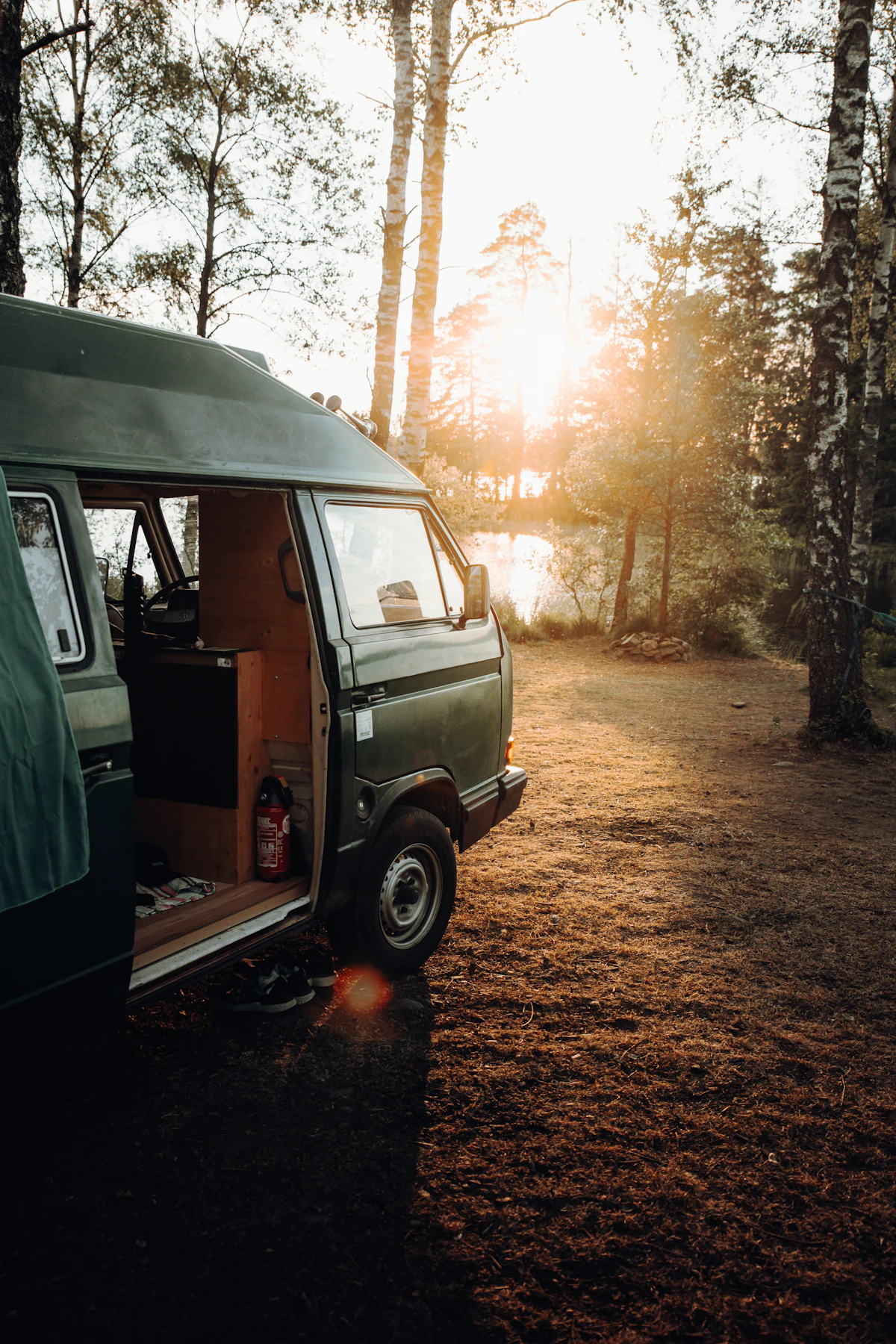 Camper van parked in a pine clearing with the door open at golden hour