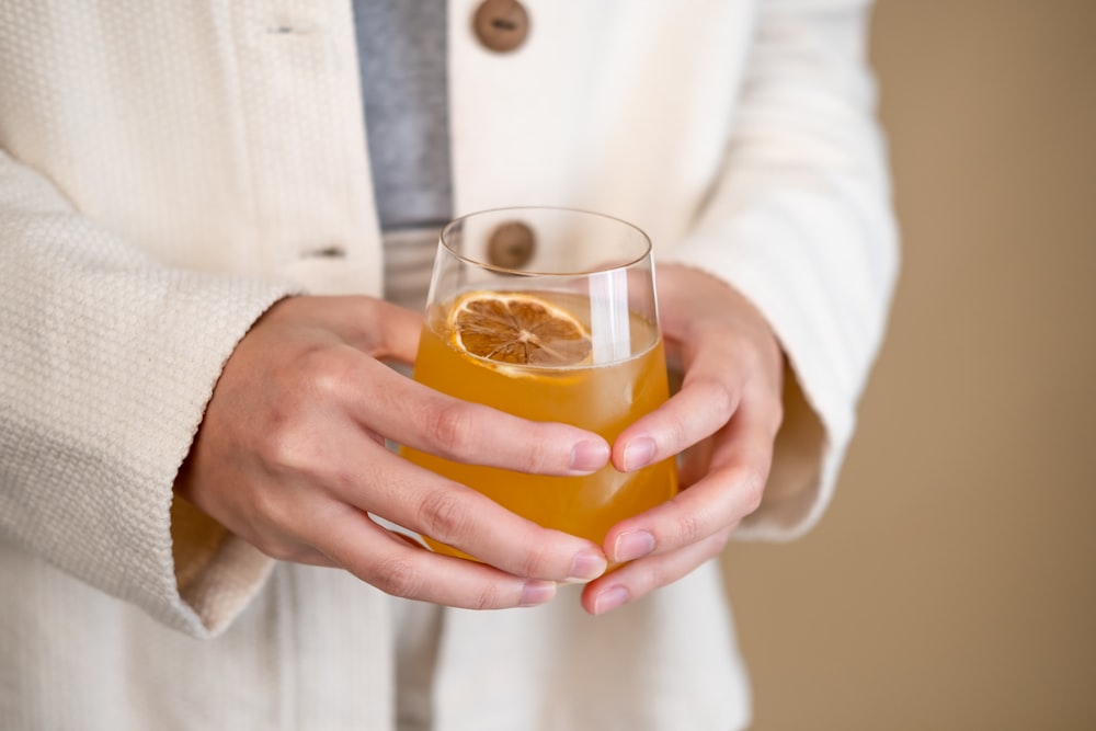 personne tenant un verre à boire transparent avec un liquide orange