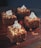 Four chocolate-covered desserts are topped with crushed nuts and a dollop of whipped cream, arranged on a dark wooden surface.
