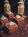 Four chocolate cakes topped with whipped cream and sprinkled with chopped nuts are arranged on a dark wooden board. In the background, there are two jars filled with creamy beverages, topped with whipped cream and drizzled with chocolate.