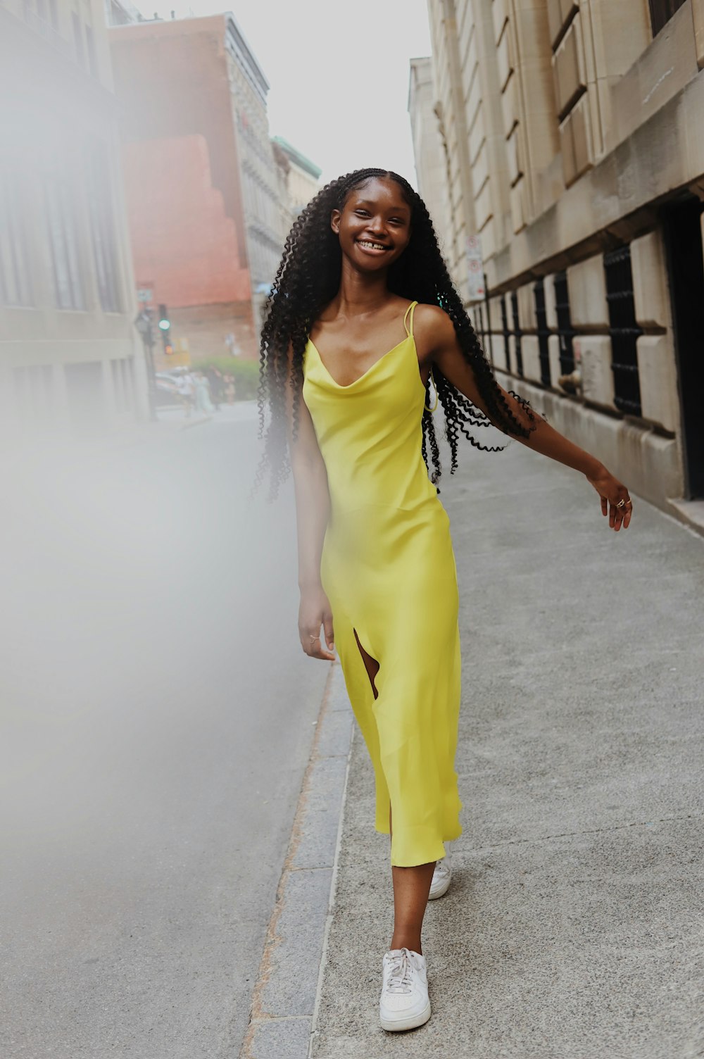 woman in yellow sleeveless dress standing on gray concrete pavement