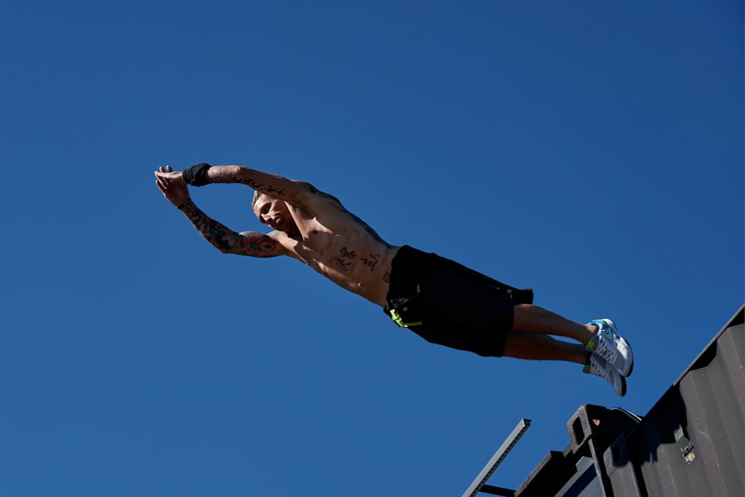 man in black shorts and black shirt jumping under blue sky during daytime