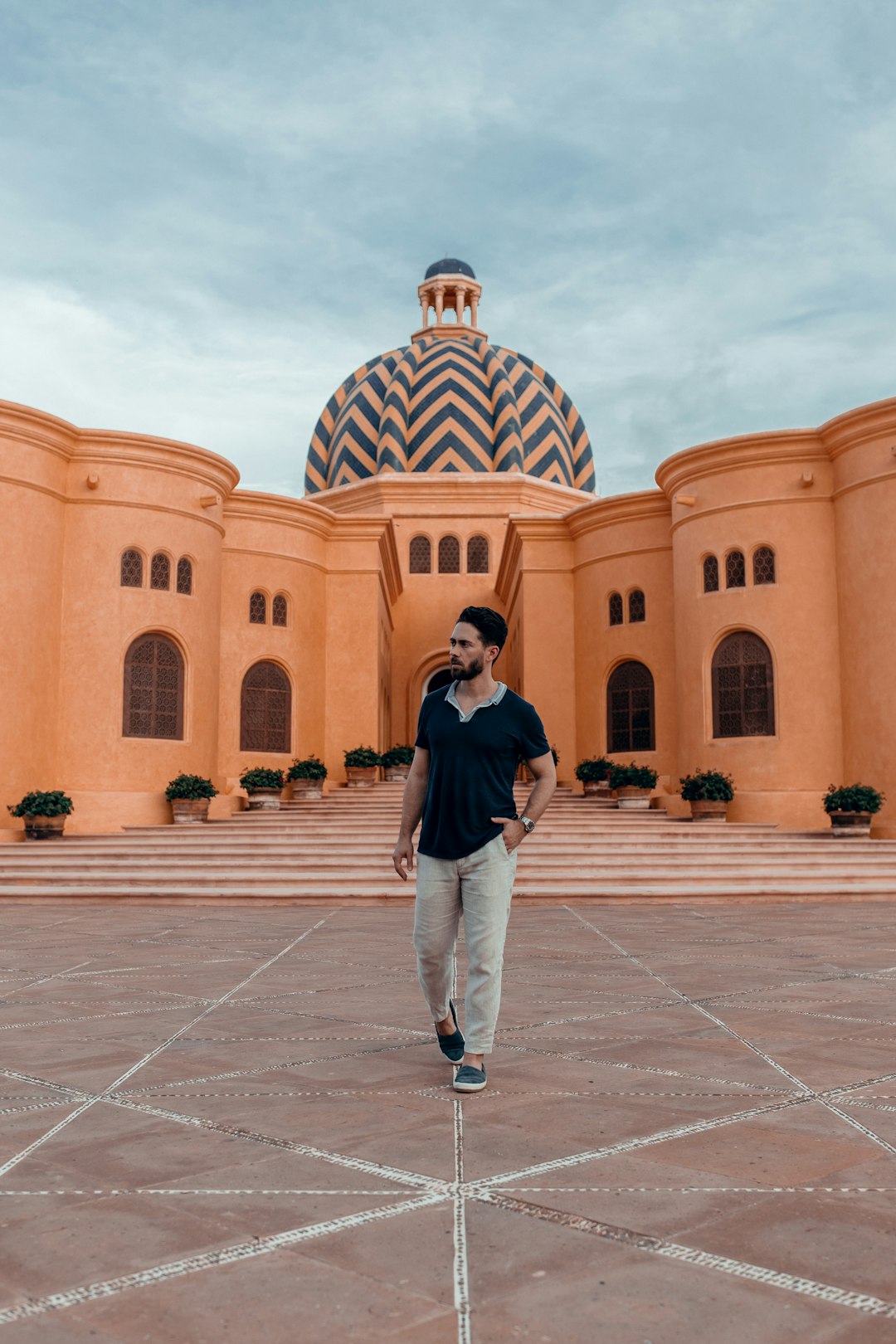 man in black jacket and white pants standing in front of brown concrete building during daytime