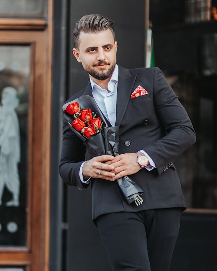 man in black suit holding red rose bouquet