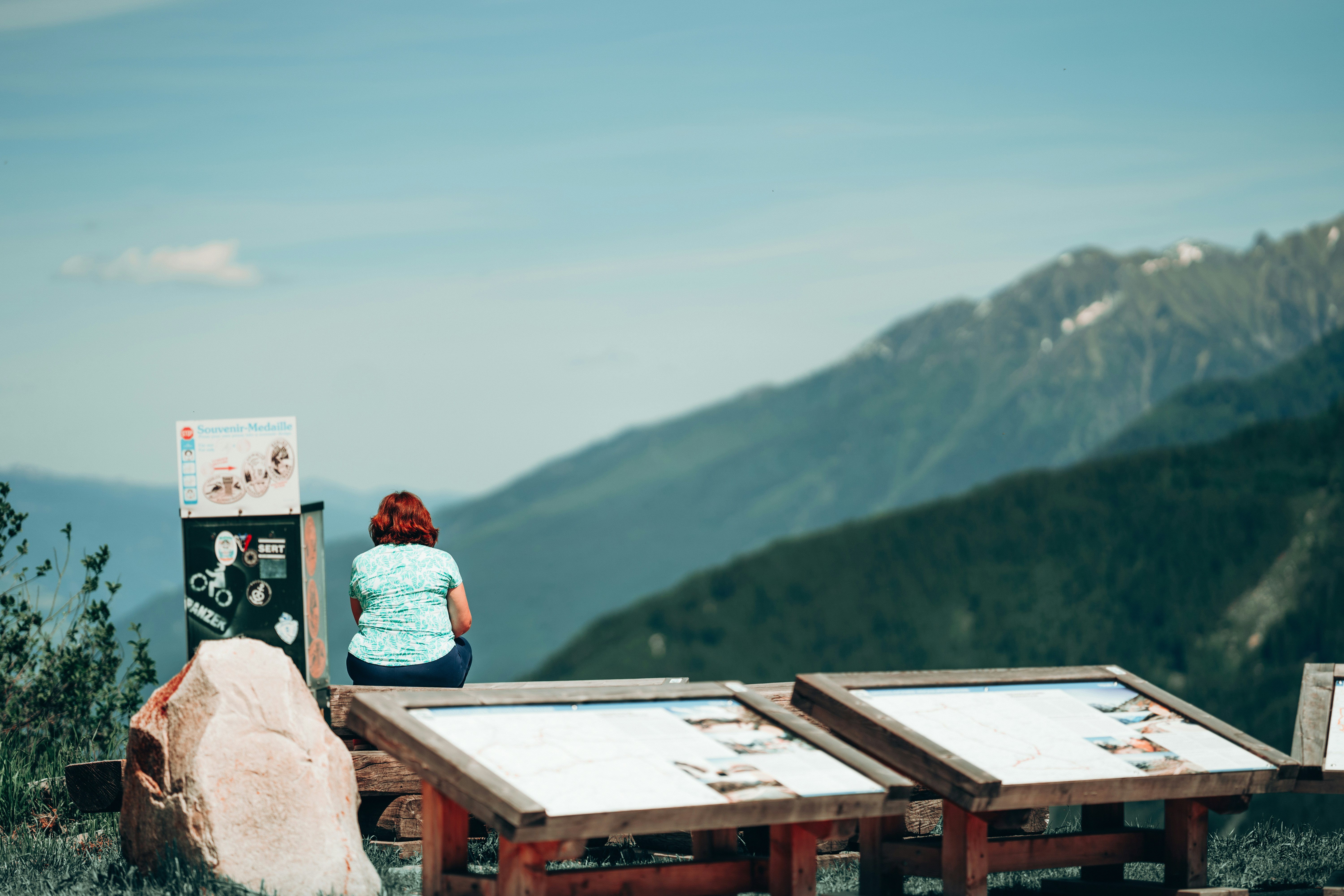 man in red and white plaid dress shirt sitting on brown wooden roof looking at mountains