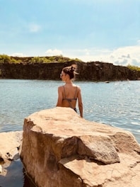 woman in brown tank top sitting on brown rock near body of water during daytime