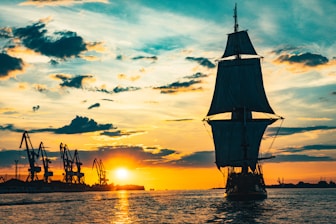 silhouette of sail ship on sea during sunset