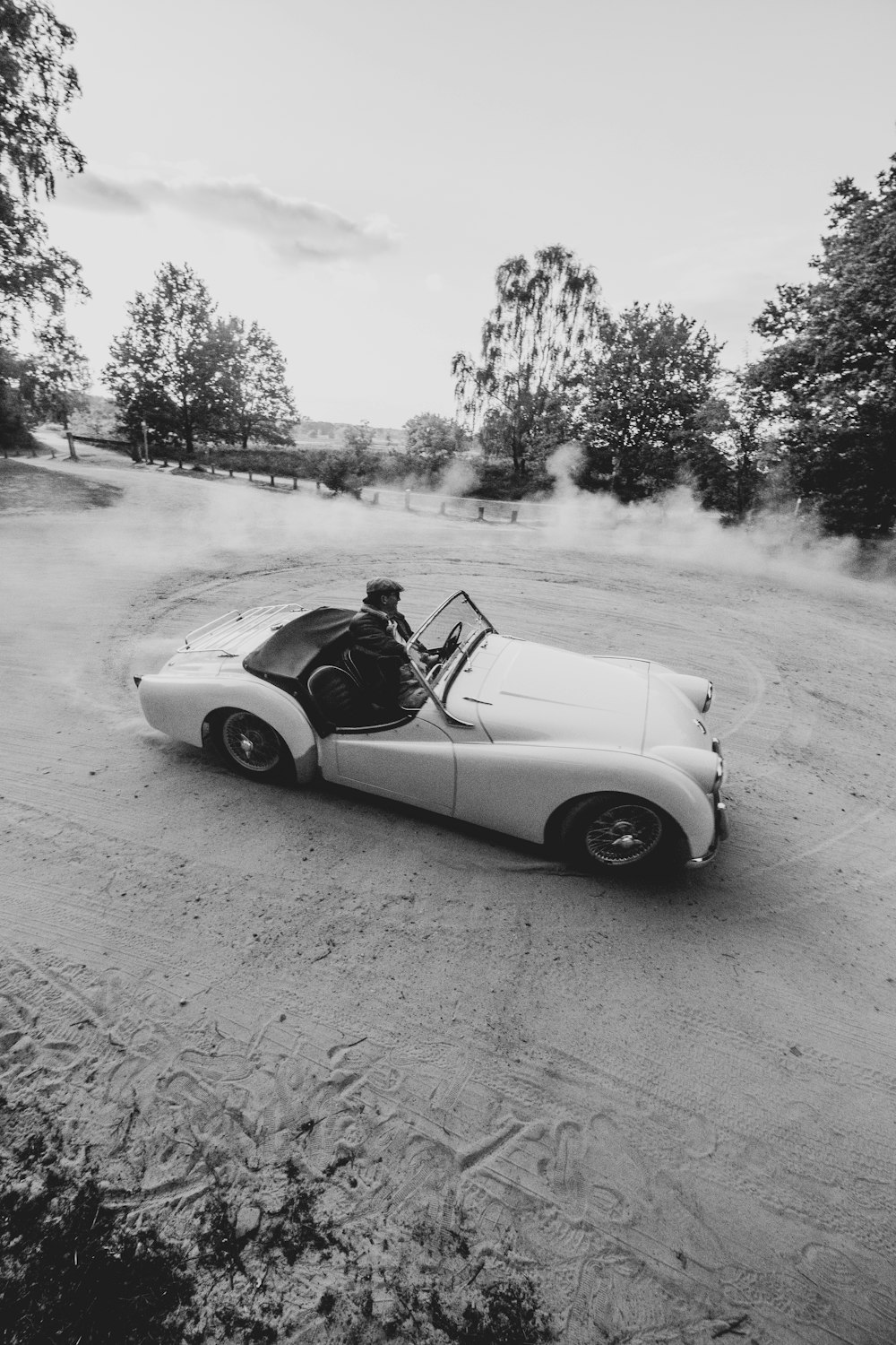 Foto en escala de grises de un hombre montando en un coche descapotable blanco