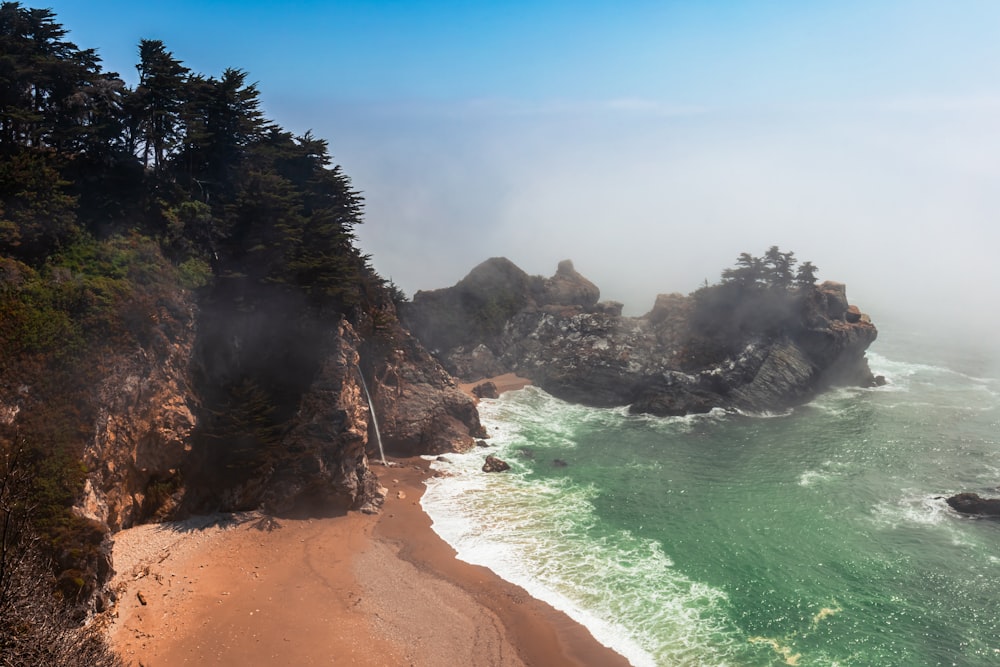 brown sand beach with green trees and brown rock formation