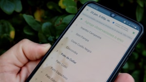 A hand is holding a smartphone, which displays a list of bird species names in Spanish against a blurred background of green leaves.