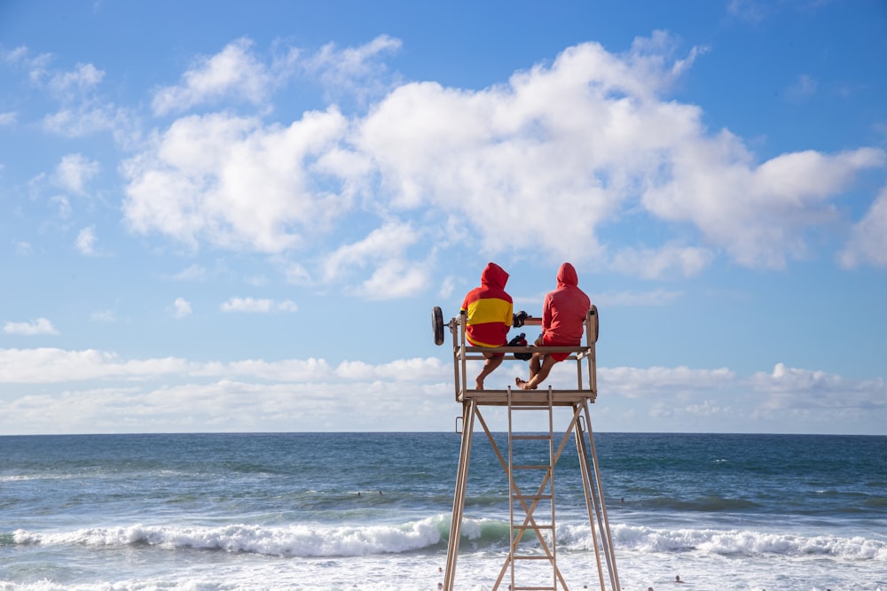 person in red hoodie sitting on brown wooden chair on beach during daytime