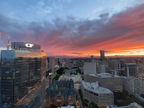 A cityscape during sunset with skyscrapers and office buildings, including a prominent tower with a 'CF' logo. The sky is filled with dramatic red and orange clouds, gradually transitioning to a darker blue as the sun sets.