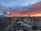 A cityscape during sunset with skyscrapers and office buildings, including a prominent tower with a 'CF' logo. The sky is filled with dramatic red and orange clouds, gradually transitioning to a darker blue as the sun sets.