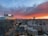 A cityscape during sunset with skyscrapers and office buildings, including a prominent tower with a 'CF' logo. The sky is filled with dramatic red and orange clouds, gradually transitioning to a darker blue as the sun sets.