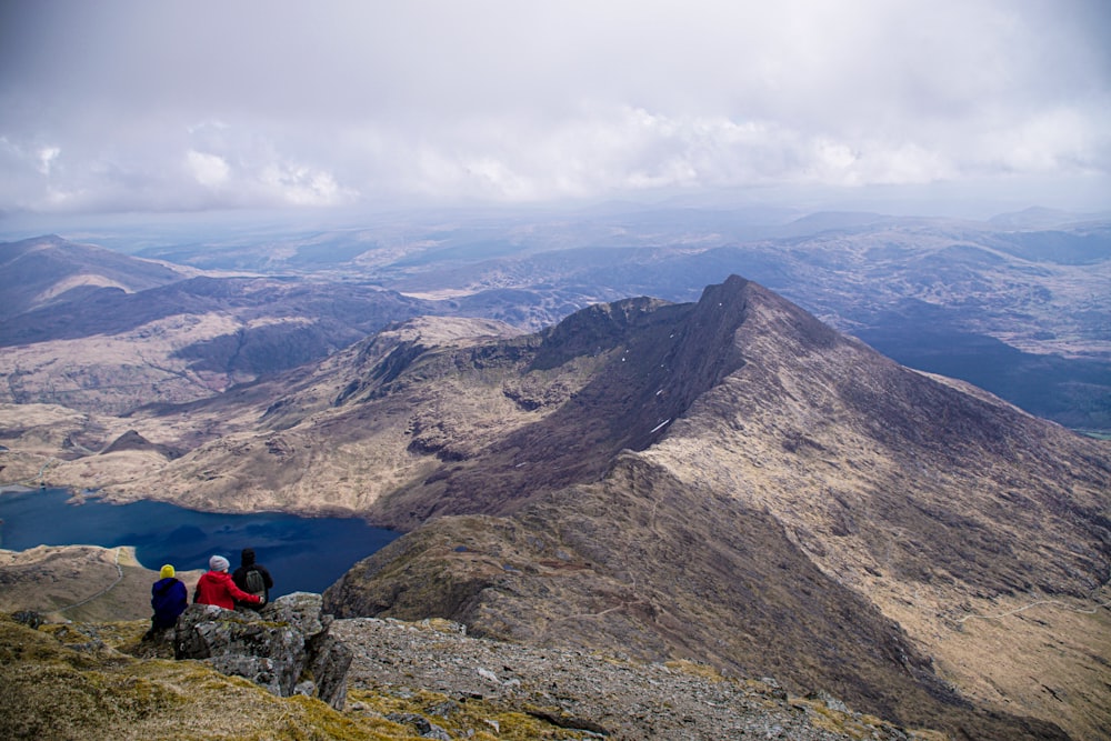 person in red jacket sitting on rock mountain during daytime