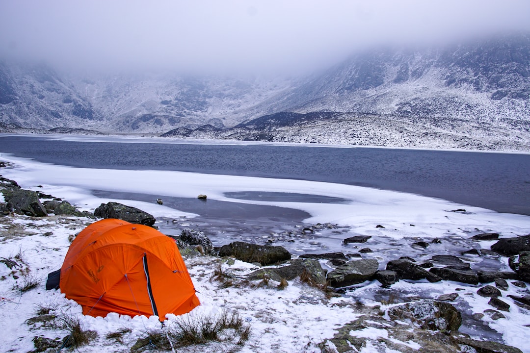 orange tent on snow covered ground near body of water during daytime