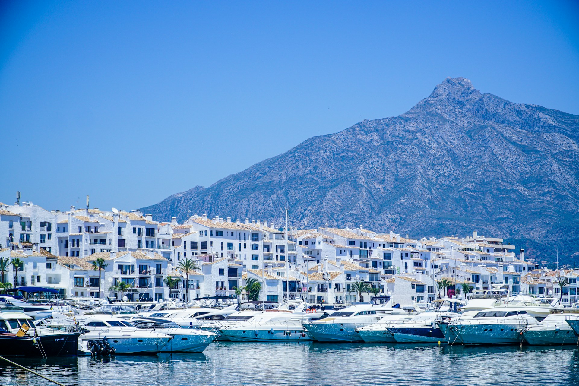 white and blue boats on sea near mountain under blue sky during daytime