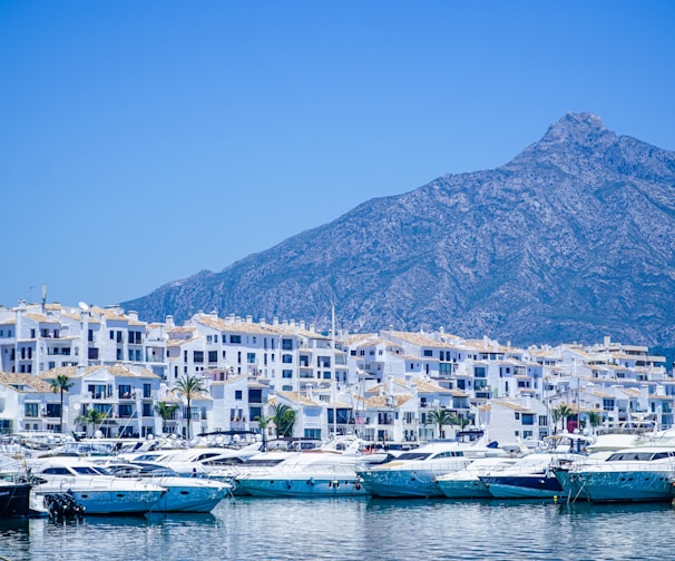 white and blue boats on sea near mountain under blue sky during daytime