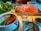 A table set for a hot pot meal with a dual-section pot containing broth, surrounded by dishes of fresh green vegetables, thinly sliced raw meat, dipping sauces, and utensils. The dining setup suggests a shared meal experience.