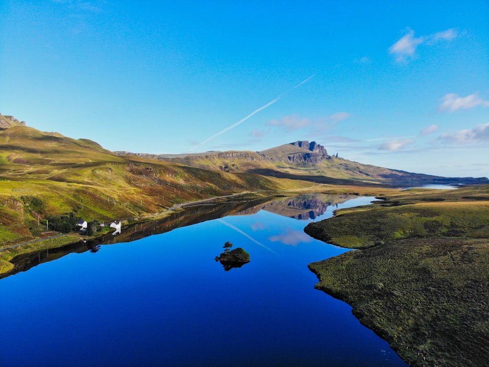 green grass covered mountain beside lake under blue sky during daytime