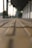 A blurred perspective of a walkway with tactile paving in the foreground and a covered walkway structure in the background. The scene appears tranquil and spacious, with subtle lighting suggesting an early morning or late afternoon setting.
