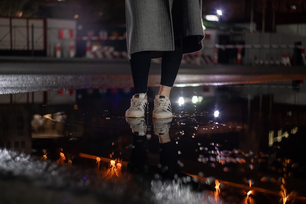 person in black pants and white shoes standing on road during night time