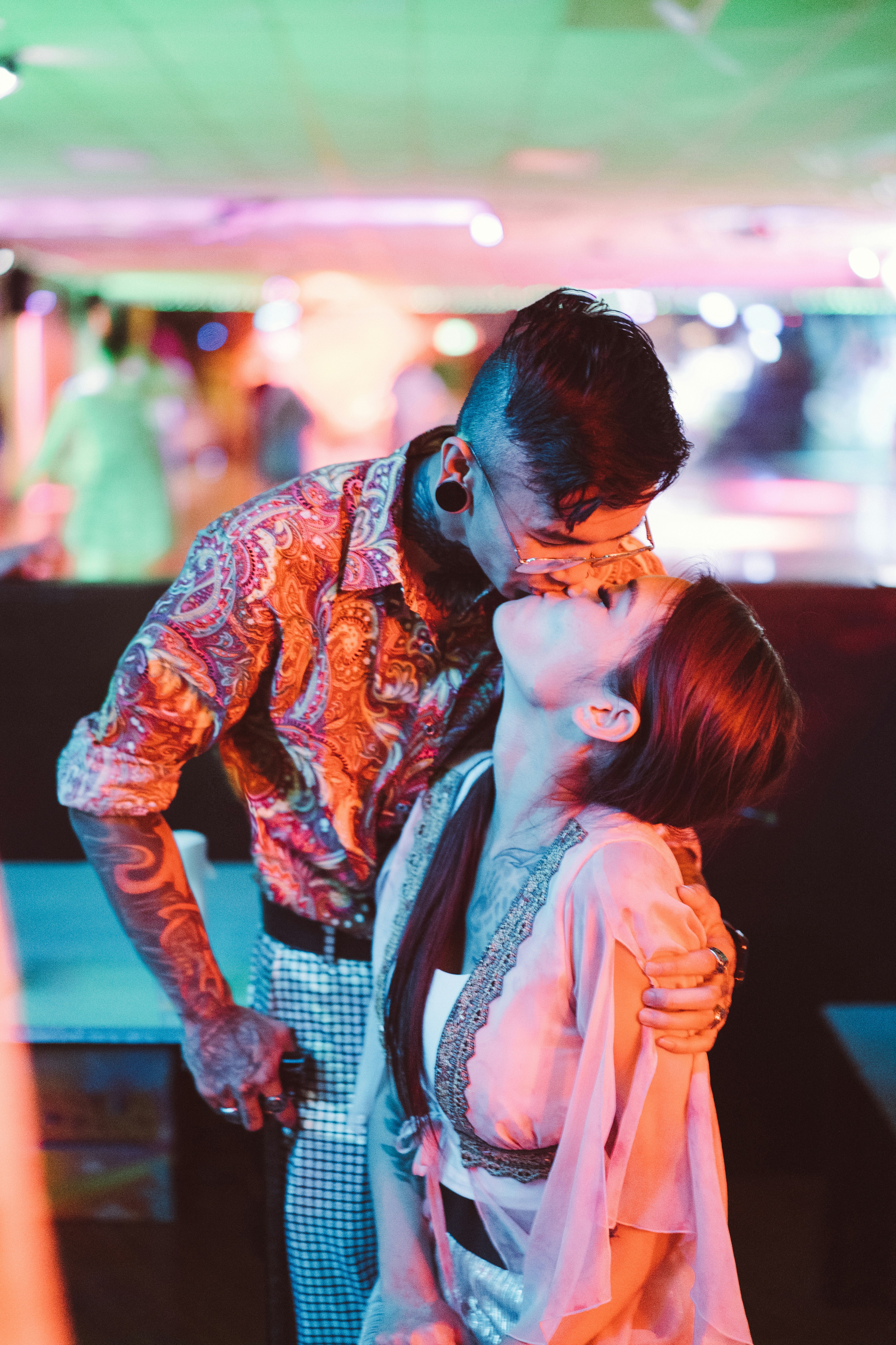 hombre en camisa de manga larga naranja y negra besando a mujer en camisa blanca sin mangas