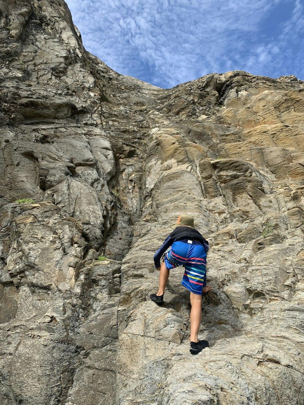 man in blue shirt climbing rocky mountain during daytime